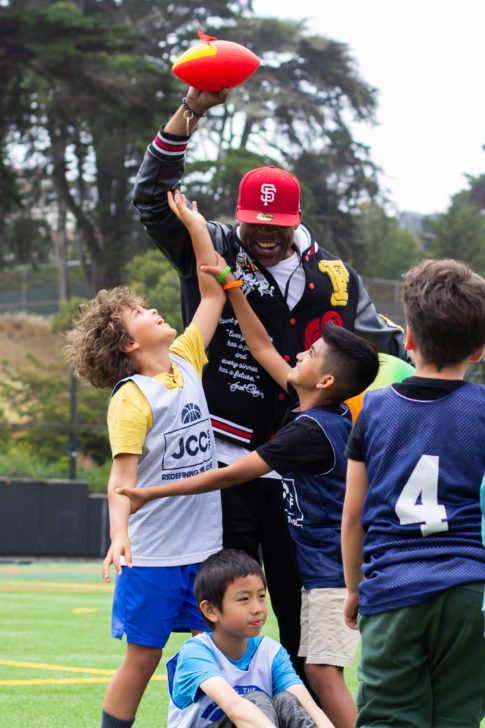 A sports instructor plays football with a group of children.