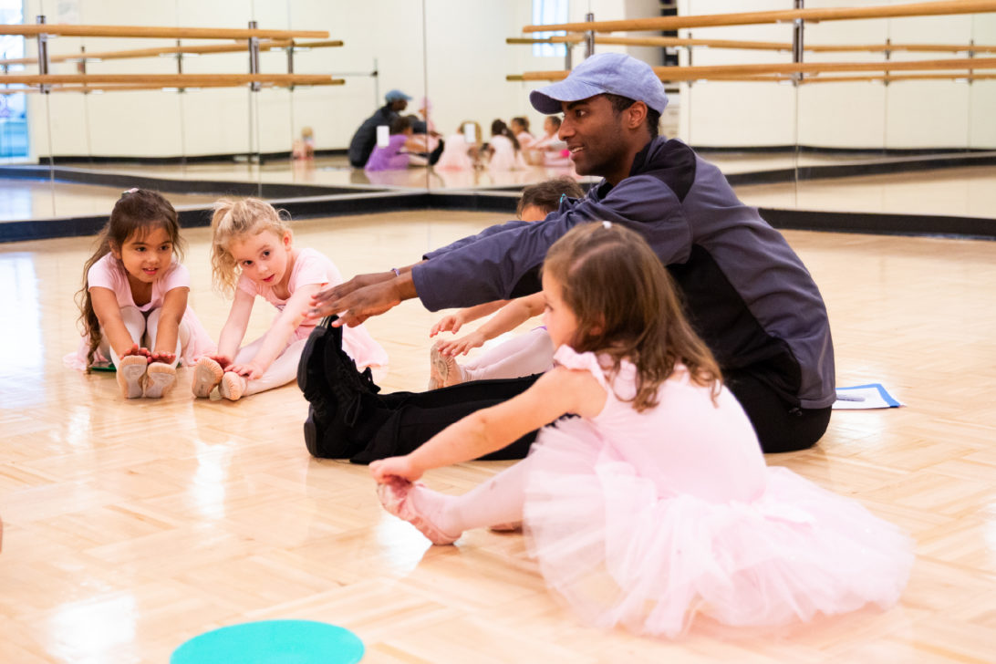 A young educator teaches ballet to a group of children.