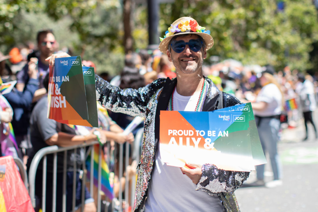 A man marches in a Pride parade, carrying sign that says "Proud to be an ally and Jewish".