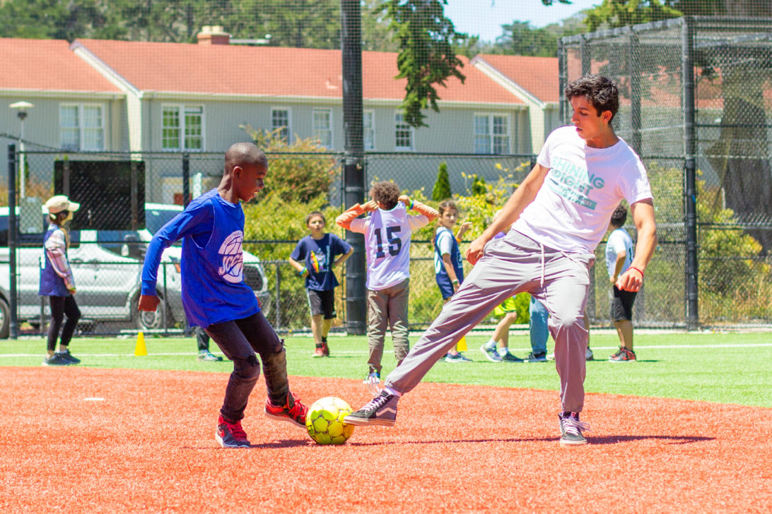 A camp counselor plays soccer with a young boy.